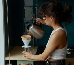 Woman pours hot water into pour-over coffee capturing her morning ritual allowing her to slow down, be more intentional and simplify life.