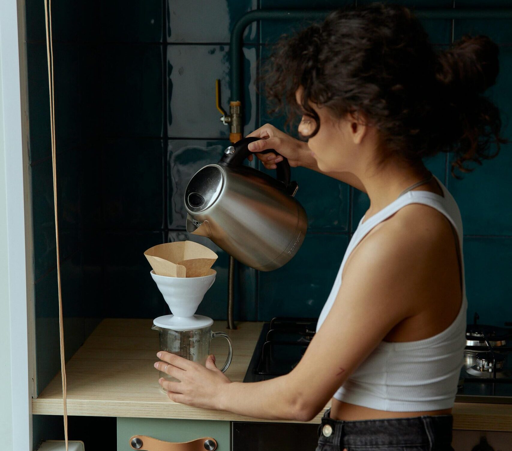 Woman pours hot water into pour-over coffee capturing her morning ritual allowing her to slow down, be more intentional and simplify life.